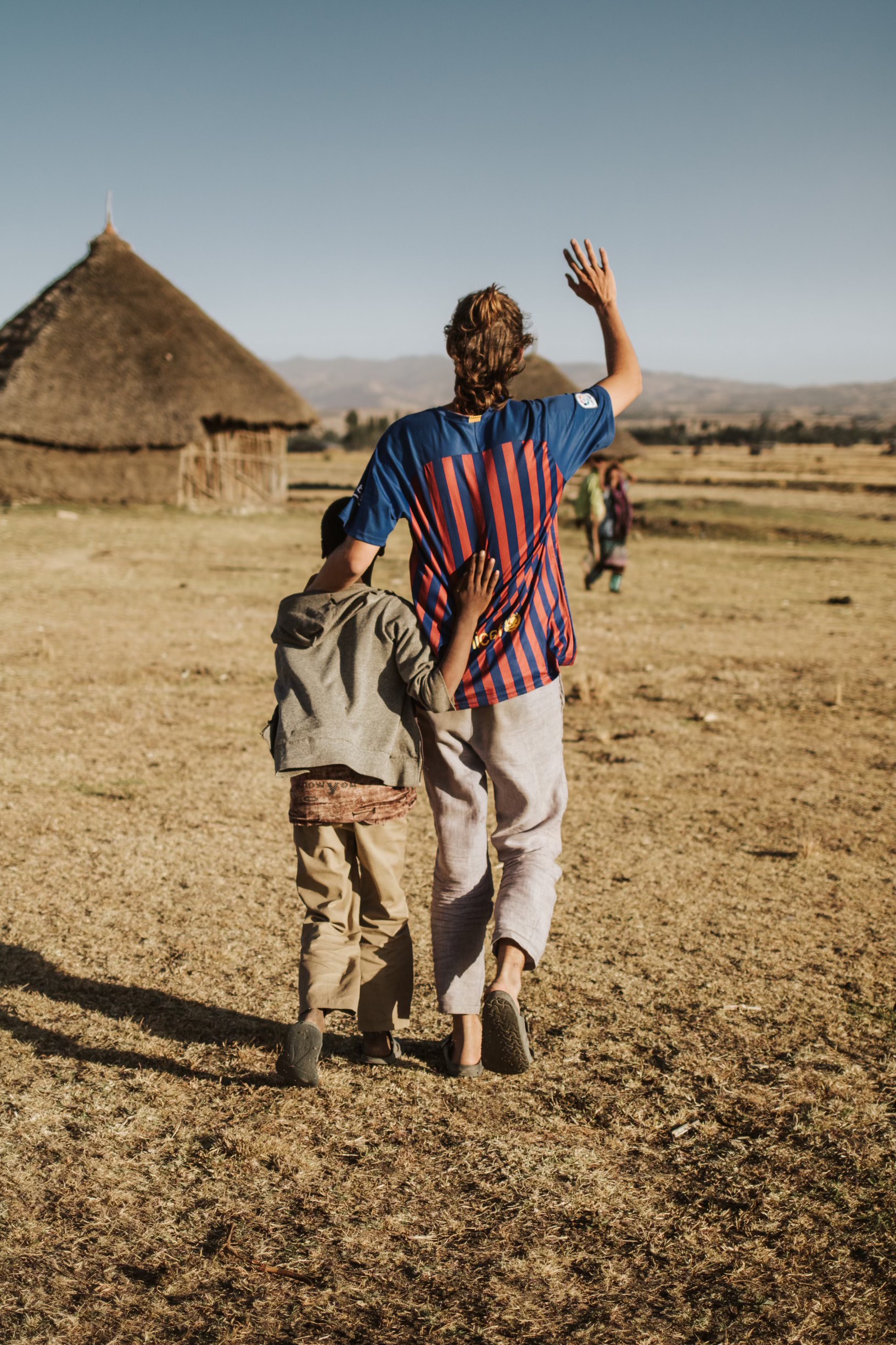 Squad member walking with a child past thatched-roof homes in Ethiopia