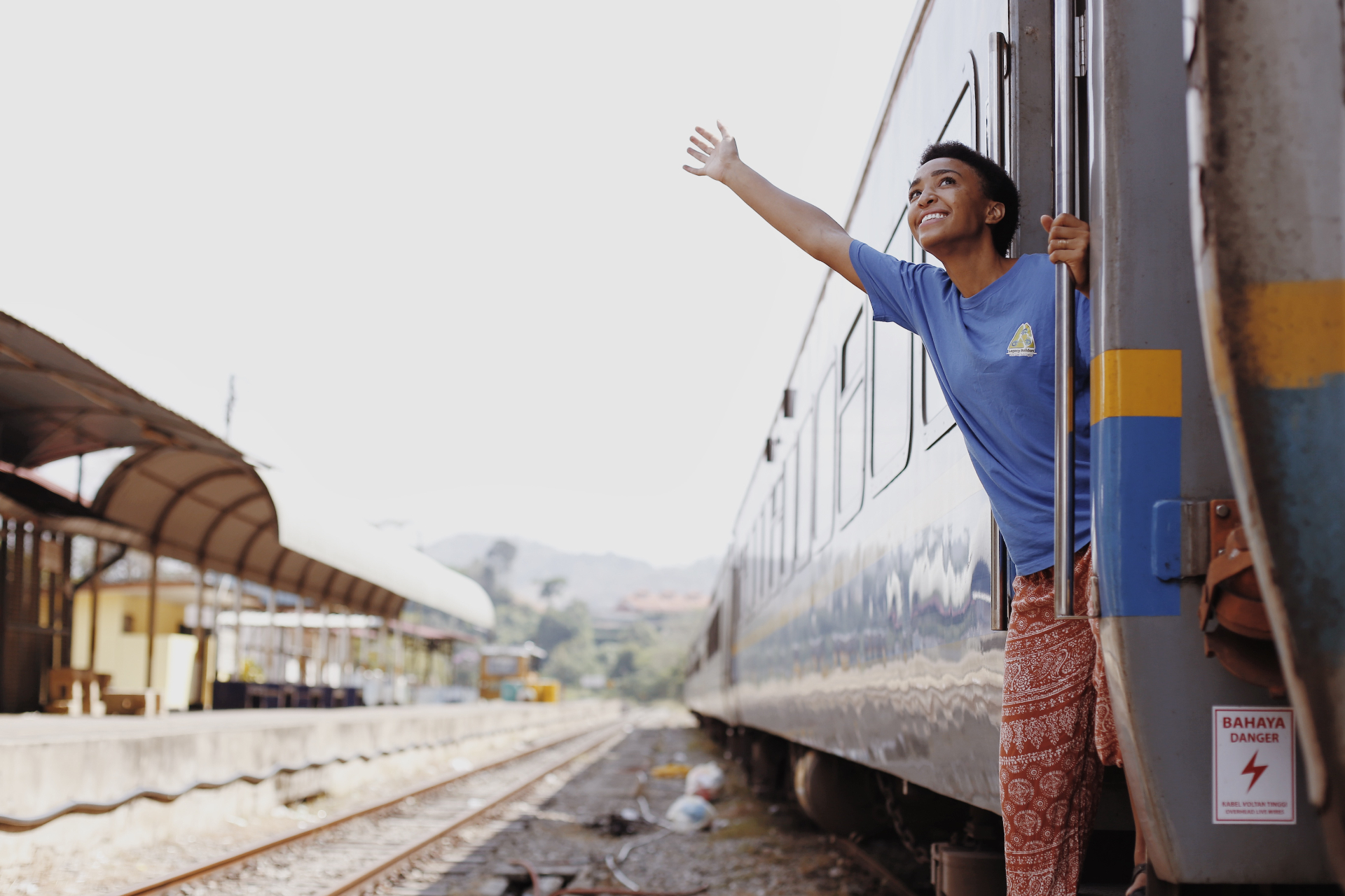 Squad member leaning out of a moving train in Malaysia with arm outstretched