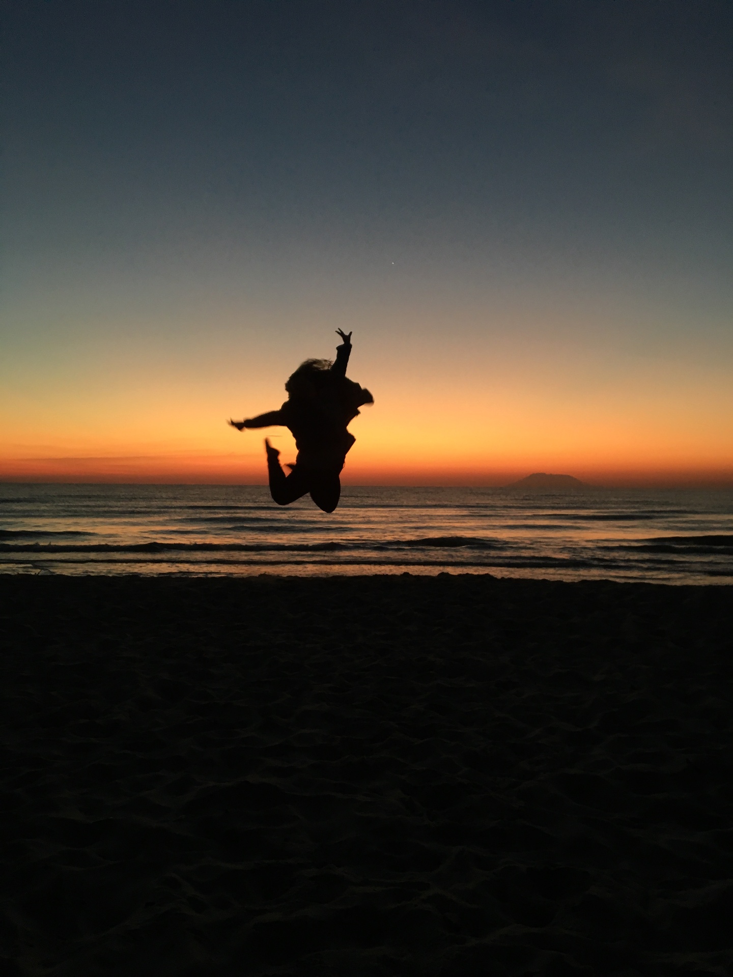 Silhouette of a student jumping on a Greek beach at sunset